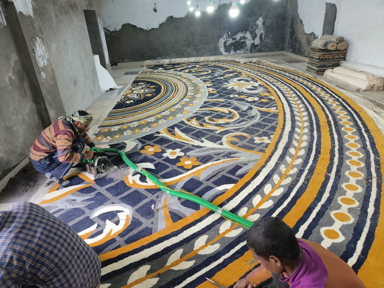 Custom luxury carpet finishing in Vadodara – craftsmen trimming hand-tufted yellow and blue rug for premium interiors.